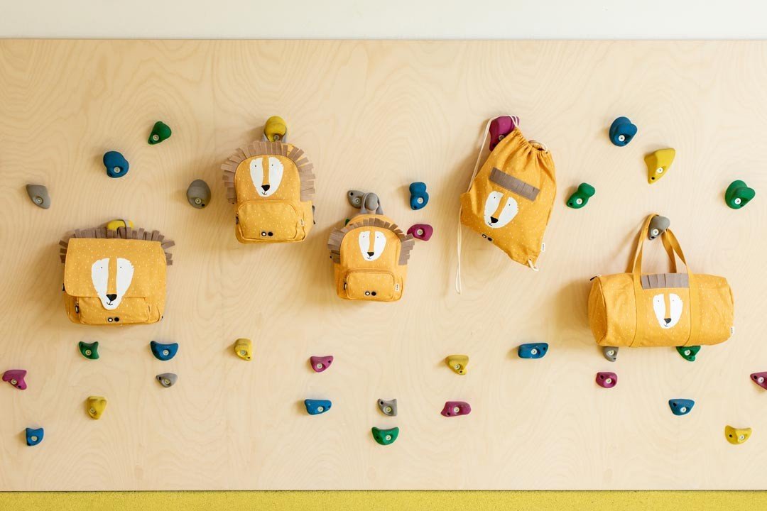 1. Collection of Trixie Baby bags including Mr. Lion drawstring bag on a wall with colorful climbing holds