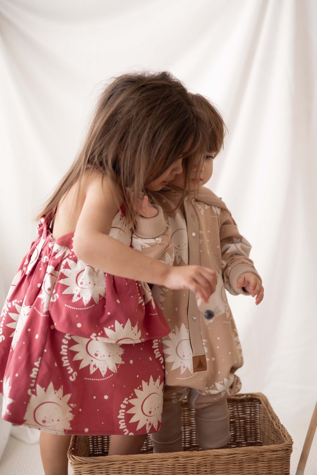 1. Two children in a basket, one wearing a pink dress with sun prints, the other in beige