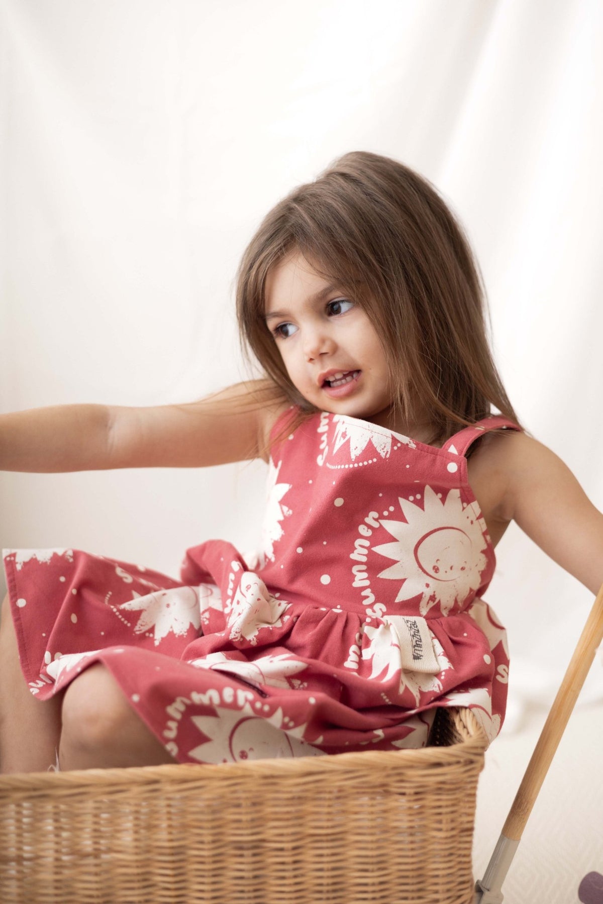 1. Girl in pink sun print dress sitting in a wicker basket with arms outstretched