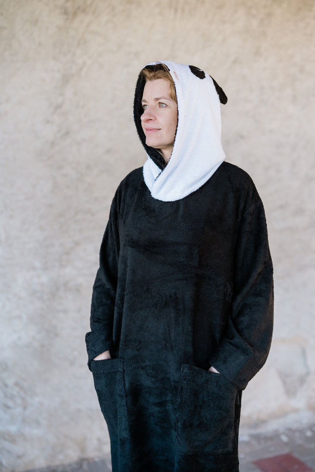 1. Unisex OEKO-TEX bamboo terry poncho by RÄTT worn by a woman, featuring panda-inspired hood and pockets, shown in lifestyle setting