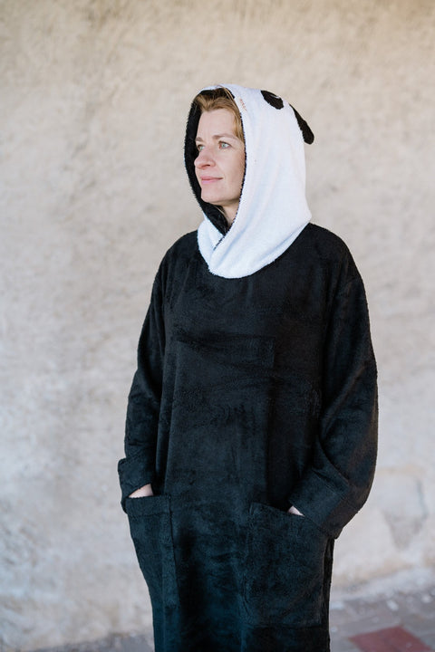 1. Unisex OEKO-TEX bamboo terry poncho by RÄTT worn by a woman, featuring panda-inspired hood and pockets, shown in lifestyle setting