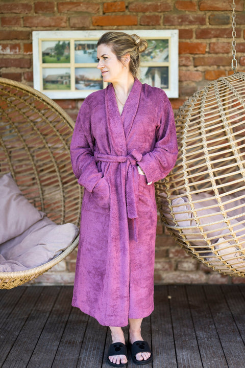5. Woman wearing a purple bamboo terry bathrobe by RÄTT, standing near hanging chairs, highlighting the robe's classic shawl collar and comfort