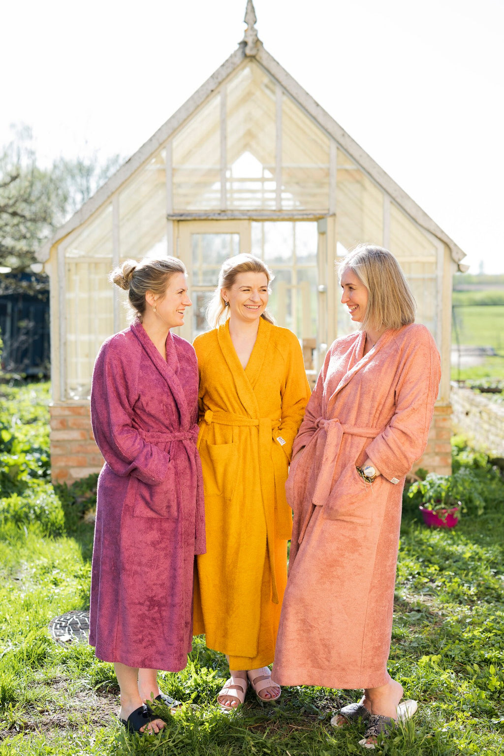 1. Women's bamboo terry bathrobes in purple, yellow, and peach worn by three women outdoors, showcasing RÄTT's luxurious and eco-friendly design