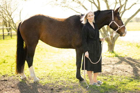 4. Woman in a black bamboo terry bathrobe by RÄTT, standing beside a horse, illustrating the robe's elegant and practical design
