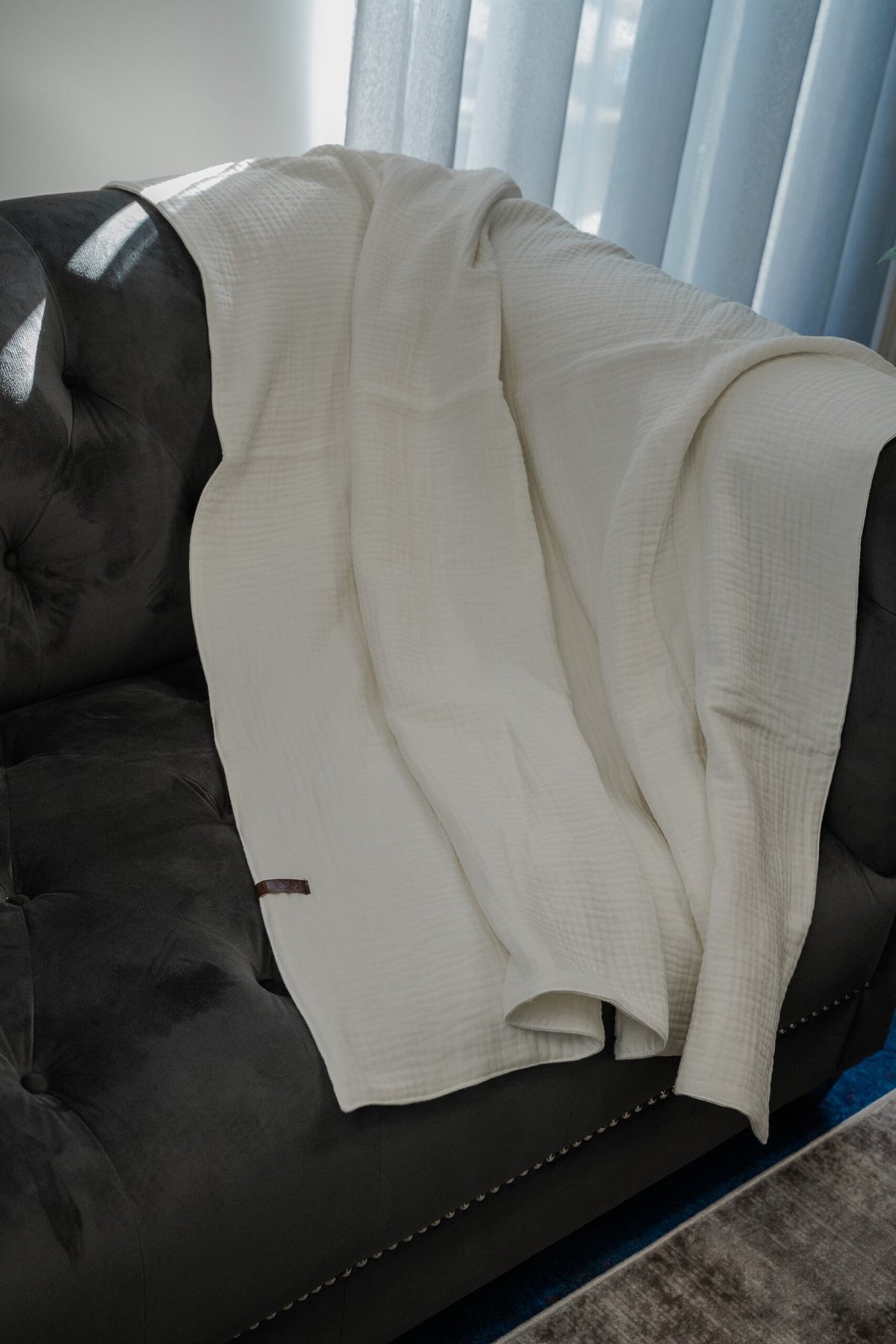 3. Ivory white muslin cotton blanket by RÄTT displayed on a sofa, emphasizing its airy and warm design