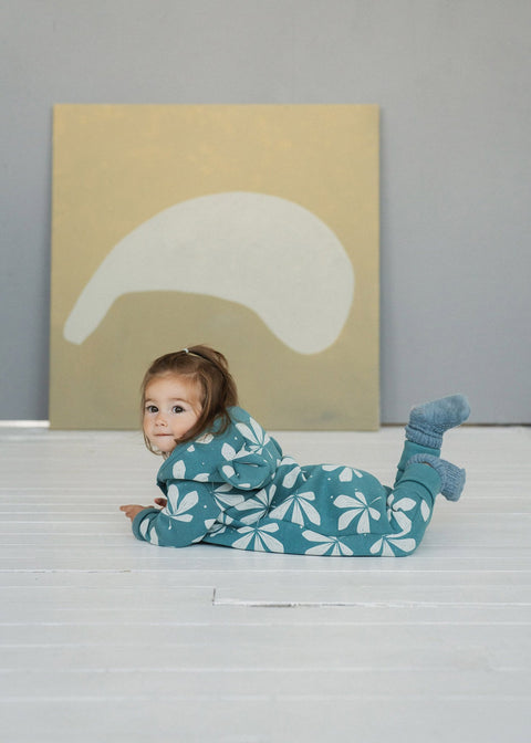 5. Toddler lying on stomach on white floor in green jumpsuit with chestnut leaf pattern and hood with ears