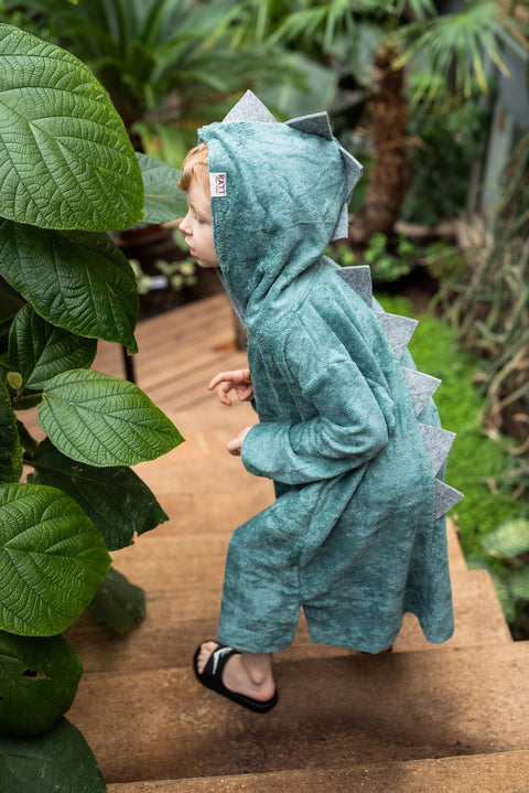 2. Toddler in green RÄTT dinosaur poncho with hood and spikes, walking up wooden steps