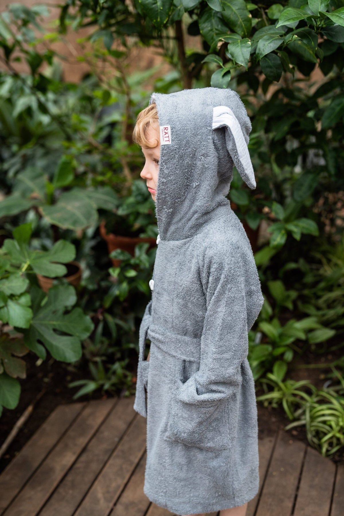 2. Side view of toddler in RÄTT bamboo terry bathrobe BUNNY with hood and belt, garden background