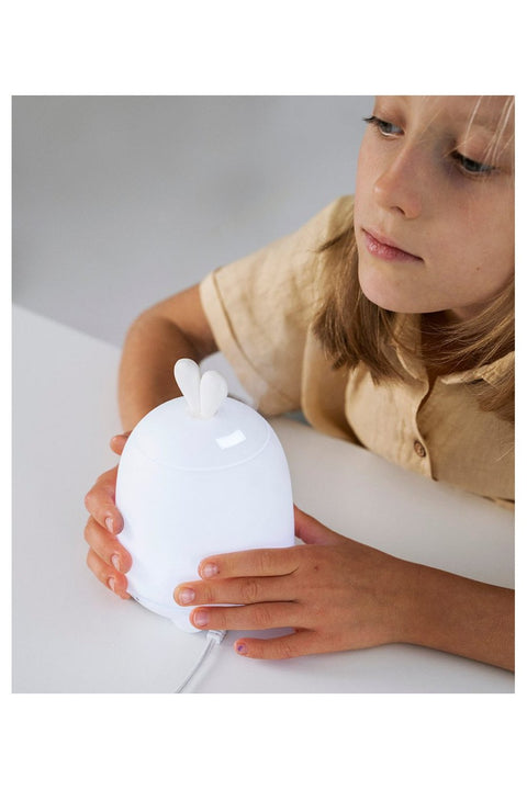 1. Child holding white Rabbit & Friends diffuser lamp with bunny ears on a table