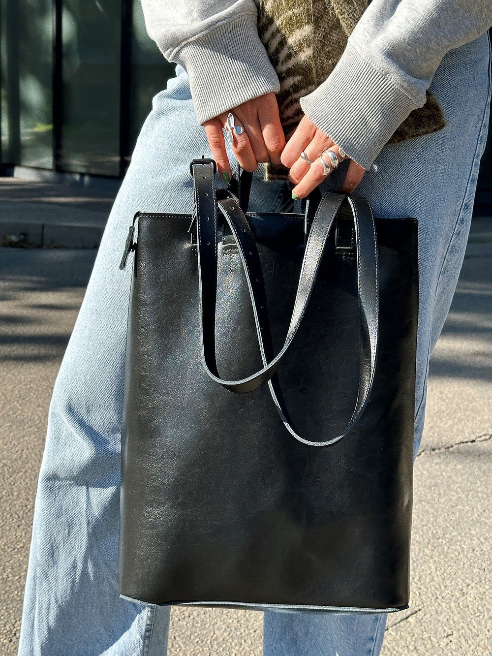 6. Close-up of woman holding RR structured tote bag in black, emphasizing handles and leather texture