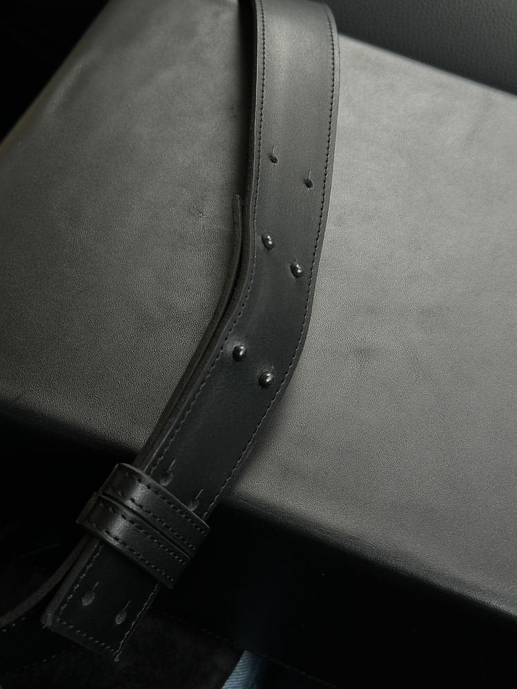 8. Close-up of black leather BOX Bag by RR, focusing on adjustable shoulder strap and painted edges