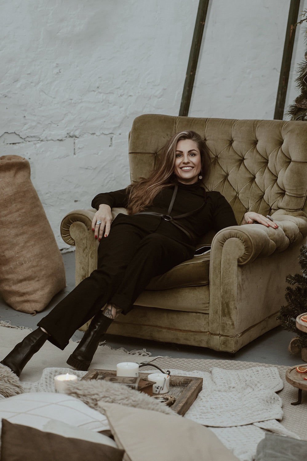 2. Woman lounging in a chair wearing a black leather body harness by RR over a black outfit, highlighting relaxed fit