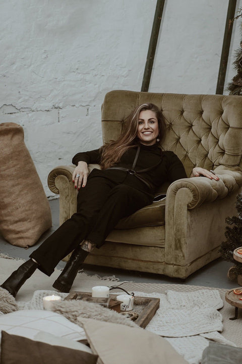 2. Woman lounging in a chair wearing a black leather body harness by RR over a black outfit, highlighting relaxed fit