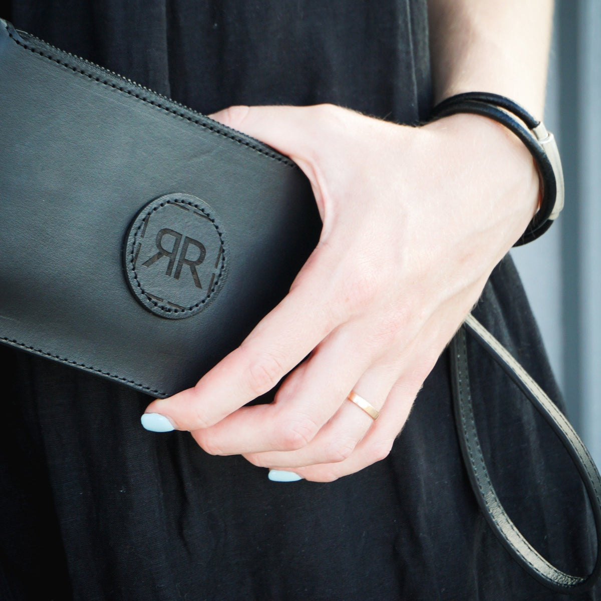 1. Woman holding RR leather wristlet wallet with elegant logo detail, showcasing minimalist design