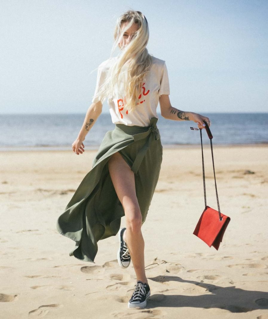 1. Woman holding RR red chain shoulder bag while walking on the beach, styled with green skirt and sneakers
