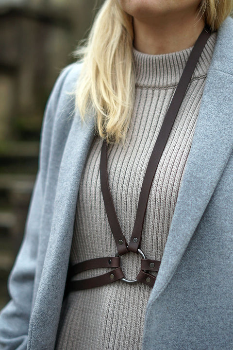 3. Close-up of brown leather body harness by RR worn over a ribbed turtleneck and grey coat, showing gunmetal details