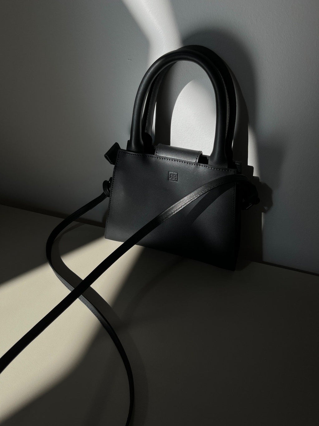 6. Close-up of RR mini leather handbag in shadow, emphasizing high-quality leather and elegant design