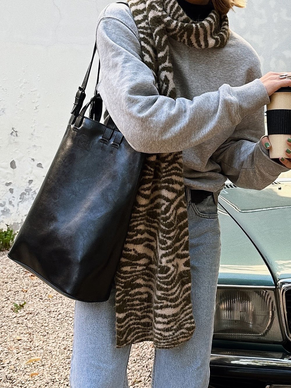 3. Woman carrying RR structured tote bag in black, paired with casual attire and scarf, near vintage car