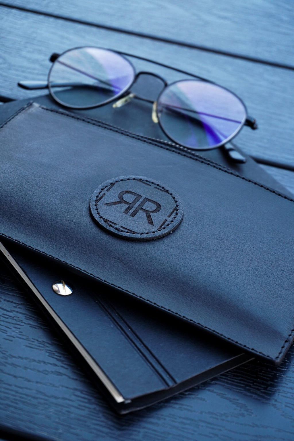 5. Close-up of RR leather wristlet wallet with glasses and notebook, highlighting logo and craftsmanship