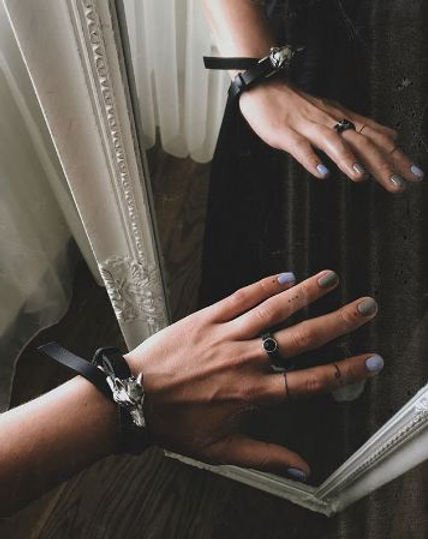 1. Women's hand wearing RR Wolf Leather Bracelet in black with silver matte wolf buckle, reflected in mirror