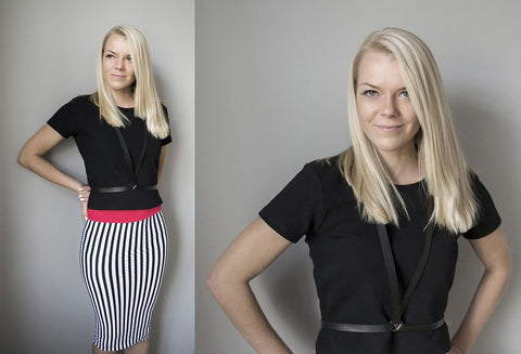 1. Women's black leather body harness by RR styled with a black top and striped skirt, studio setting