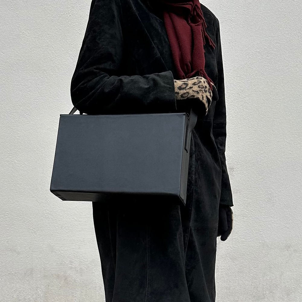 3. Women's black leather BOX Bag by RR carried by top handle, paired with a black coat and leopard print gloves