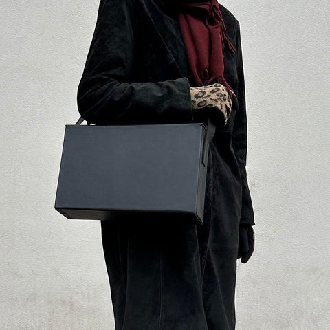 3. Women's black leather BOX Bag by RR carried by top handle, paired with a black coat and leopard print gloves