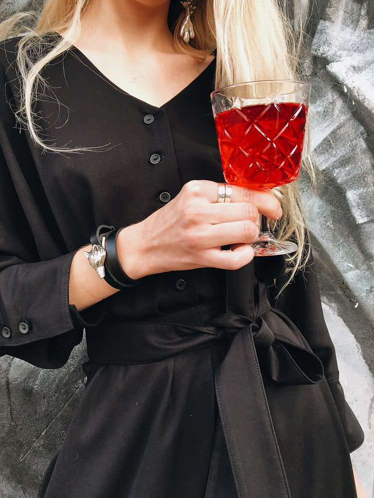 3. Woman holding a glass, wearing RR Wolf Leather Bracelet in black with silver wolf buckle