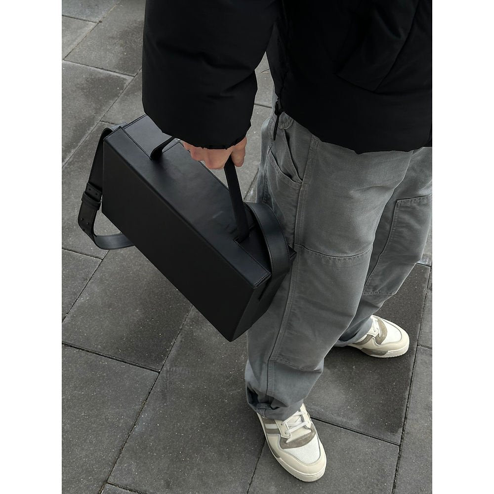 4. Men's black leather BOX Bag by RR carried by top handle, styled with grey pants and sneakers