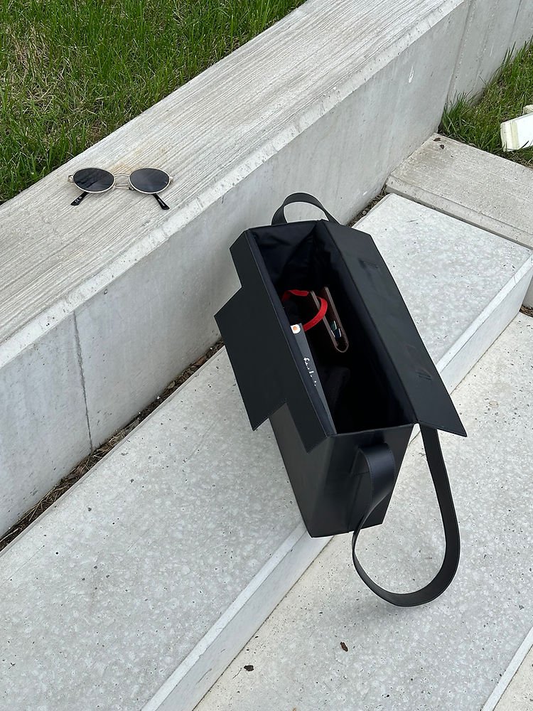 7. Black leather BOX Bag by RR on concrete steps, open to show interior with sunglasses nearby