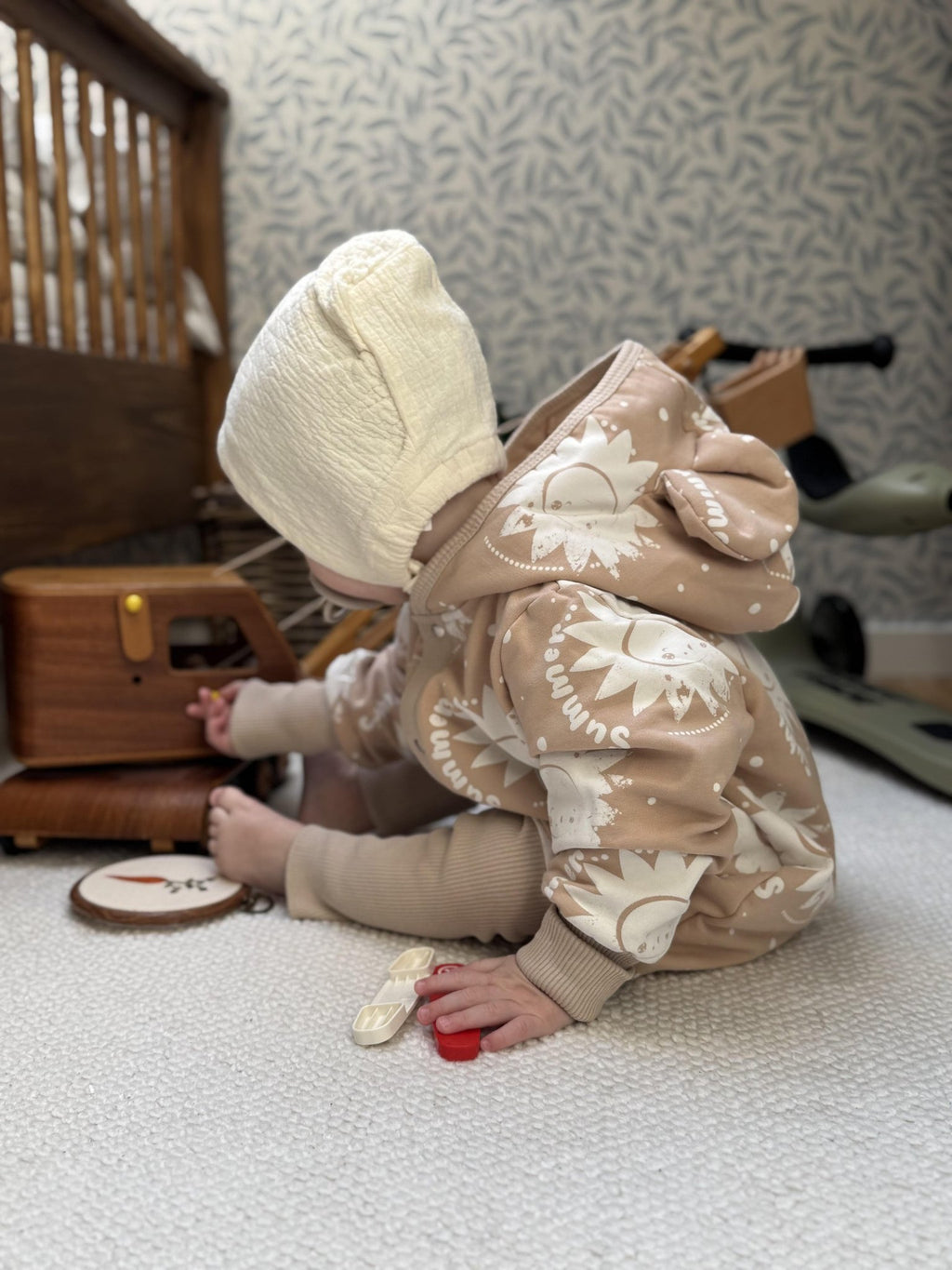 1. Baby wearing beige sun-printed jumpsuit with hood and ears, playing on carpeted floor
