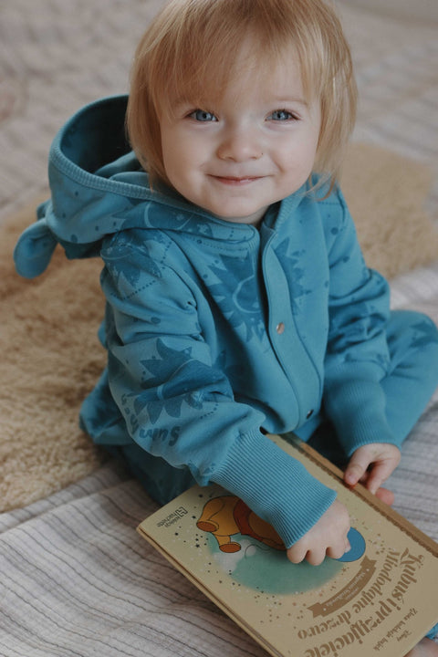 4. Child sitting on a bed wearing blue Zezuzulla eared jumpsuit, holding a book