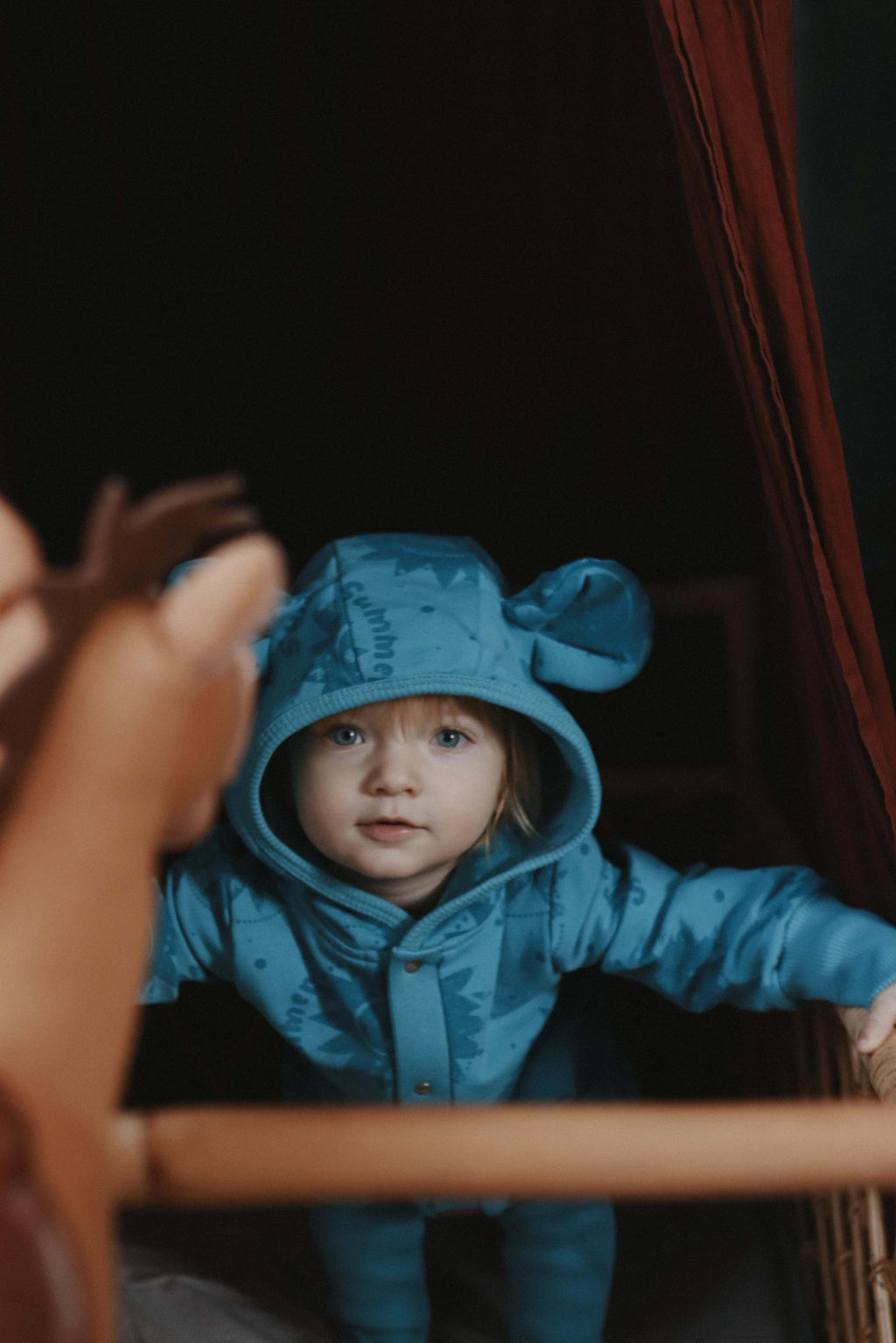 3. Child in blue Zezuzulla eared jumpsuit with sun print, peeking from behind a curtain