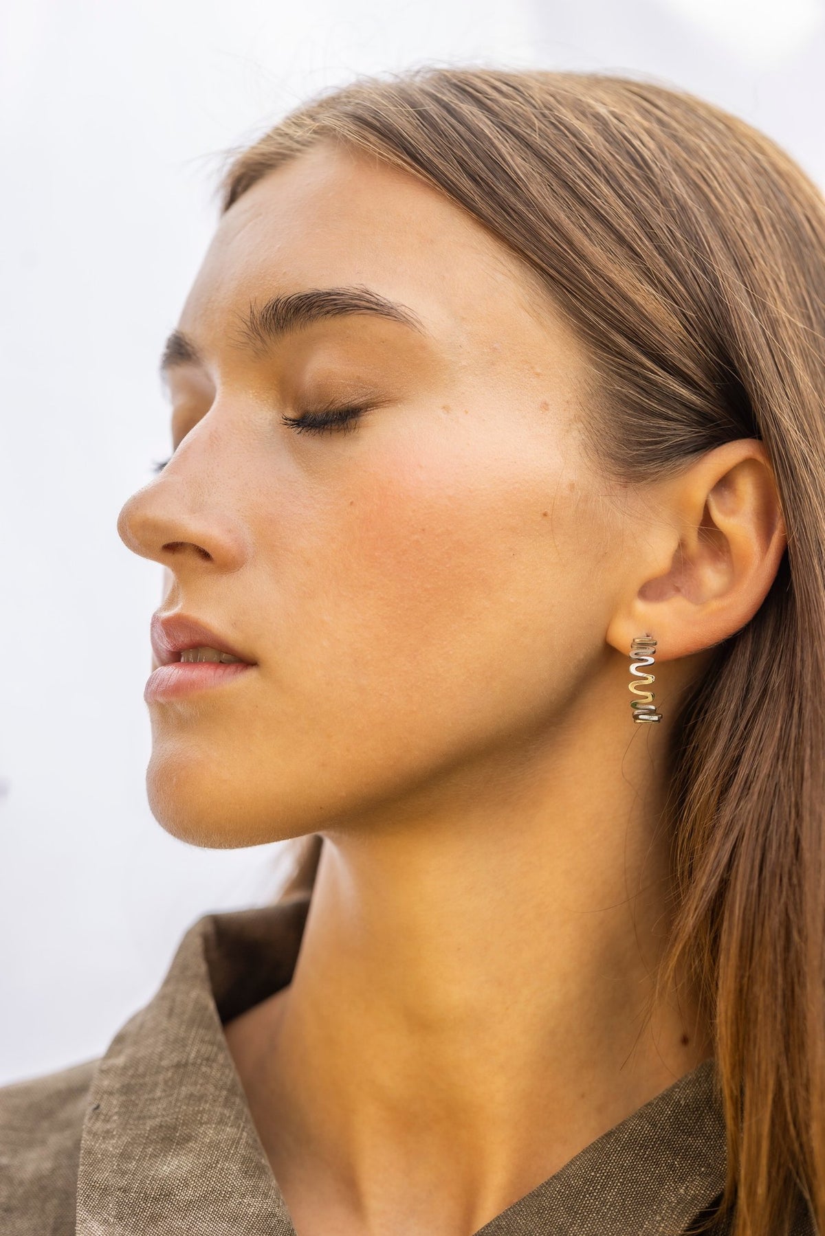 1. Woman with closed eyes wearing Lentsius stainless steel wavy hoop earring, side profile, in natural light