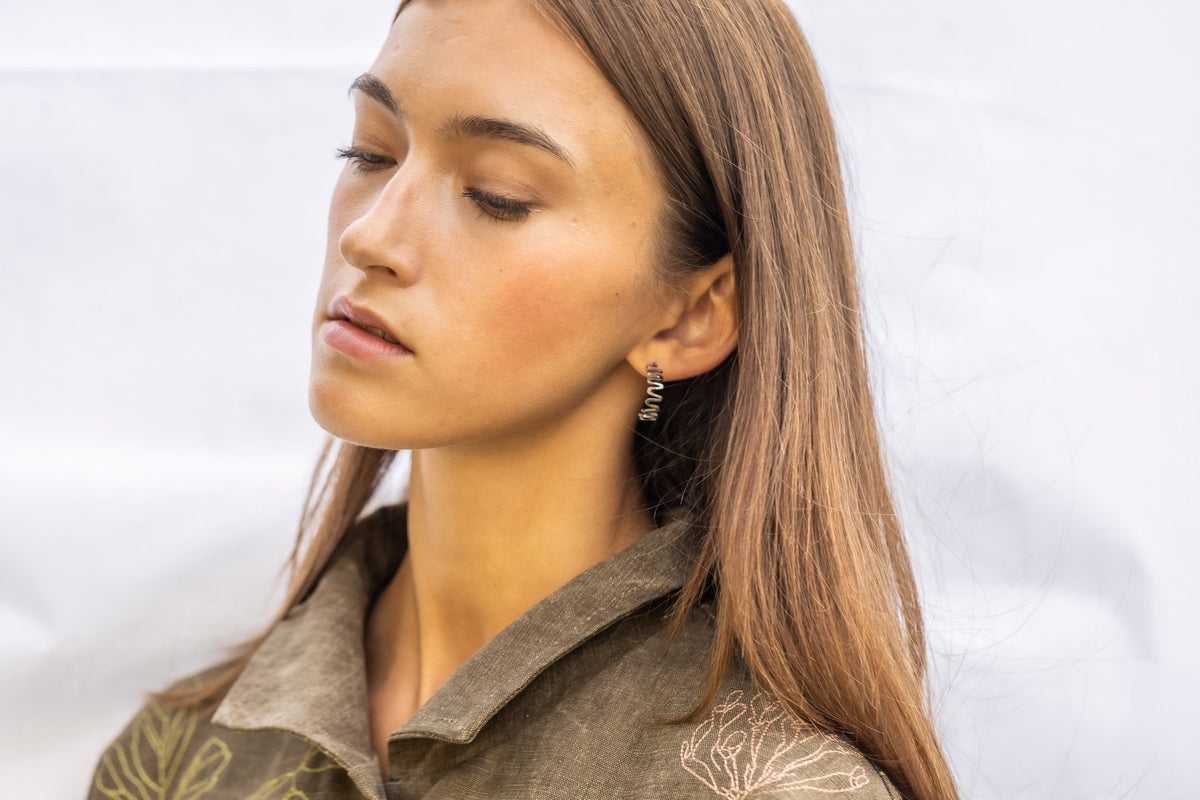 1. Woman wearing Lentsius stainless steel wavy hoop earring, looking down, in natural light