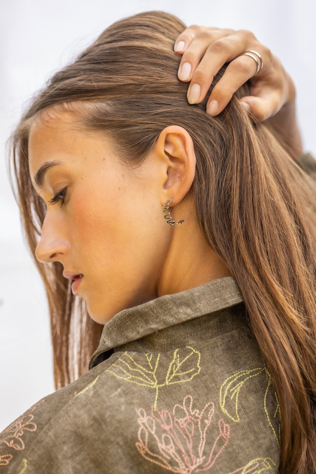 1. Woman with hand on head wearing Lentsius stainless steel wavy hoop earring, side profile, in natural light