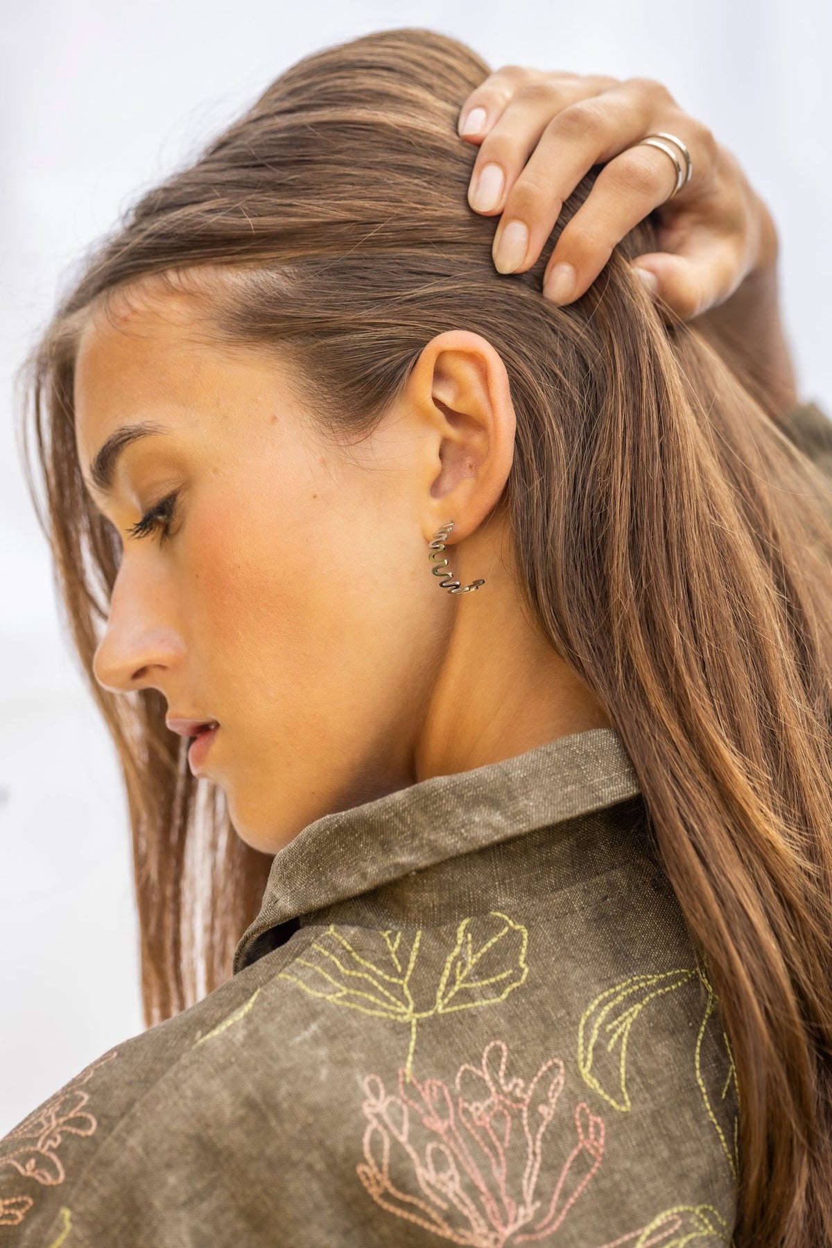 1. Woman with hand on head wearing Lentsius stainless steel wavy hoop earring, side profile, in natural light