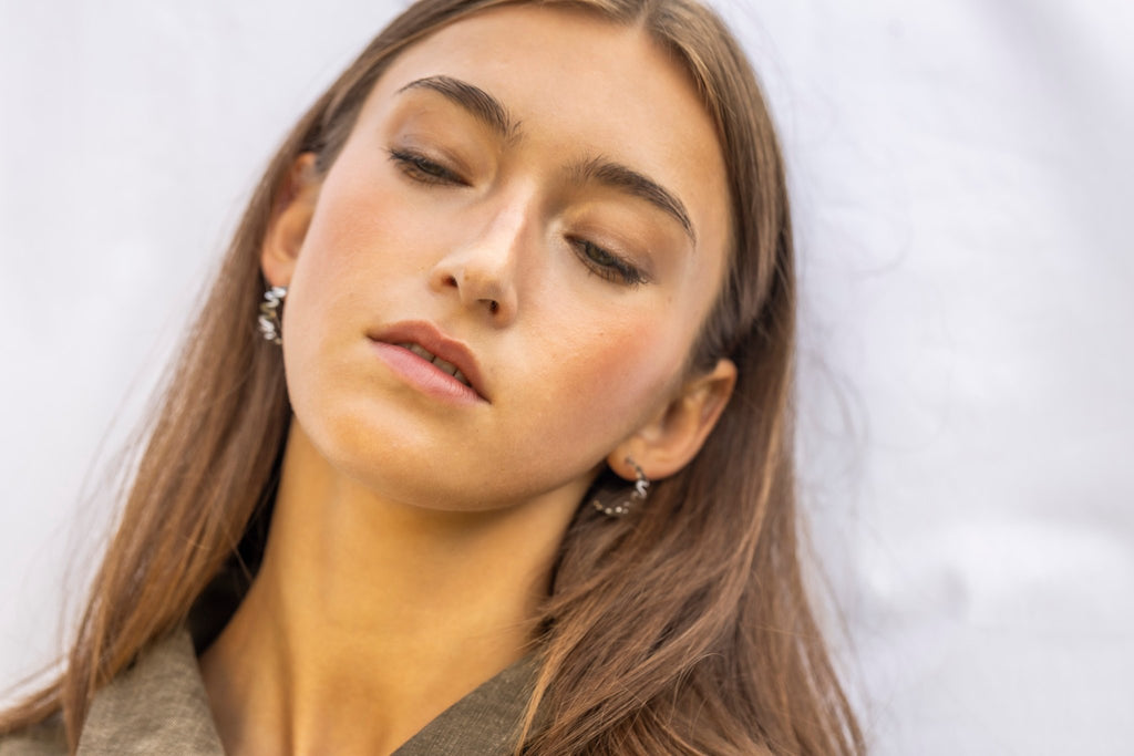 1. Woman wearing Lentsius stainless steel wavy hoop earrings, eyes closed, in natural light