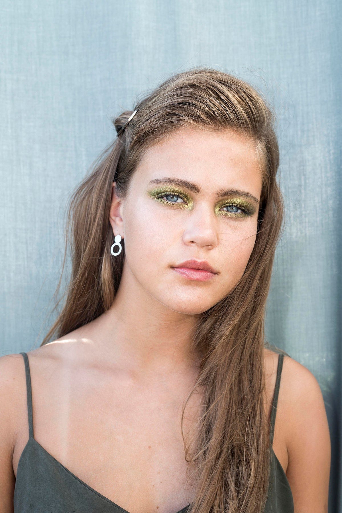 1. Woman wearing Lentsius silver stainless steel earrings with brushed finish against a blue background