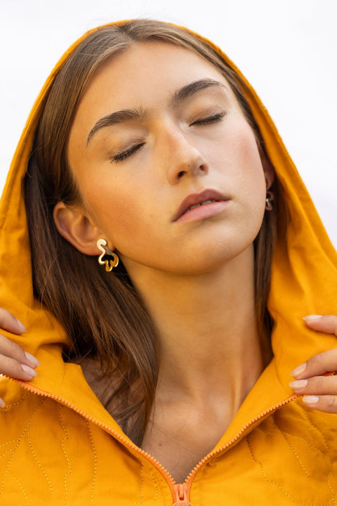 1. Woman in orange hooded jacket wearing Lentsius Folia Bold earrings, highlighting stainless steel design
