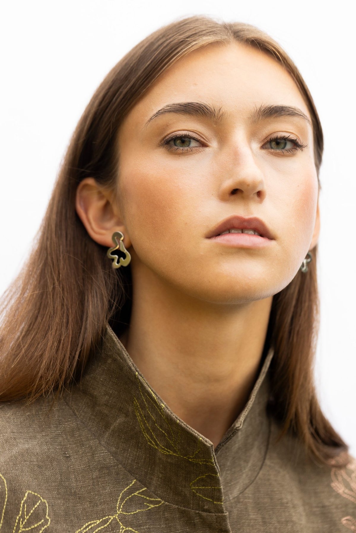 1. Woman with neutral expression wearing Lentsius Folia Bold earrings, showcasing polished finish