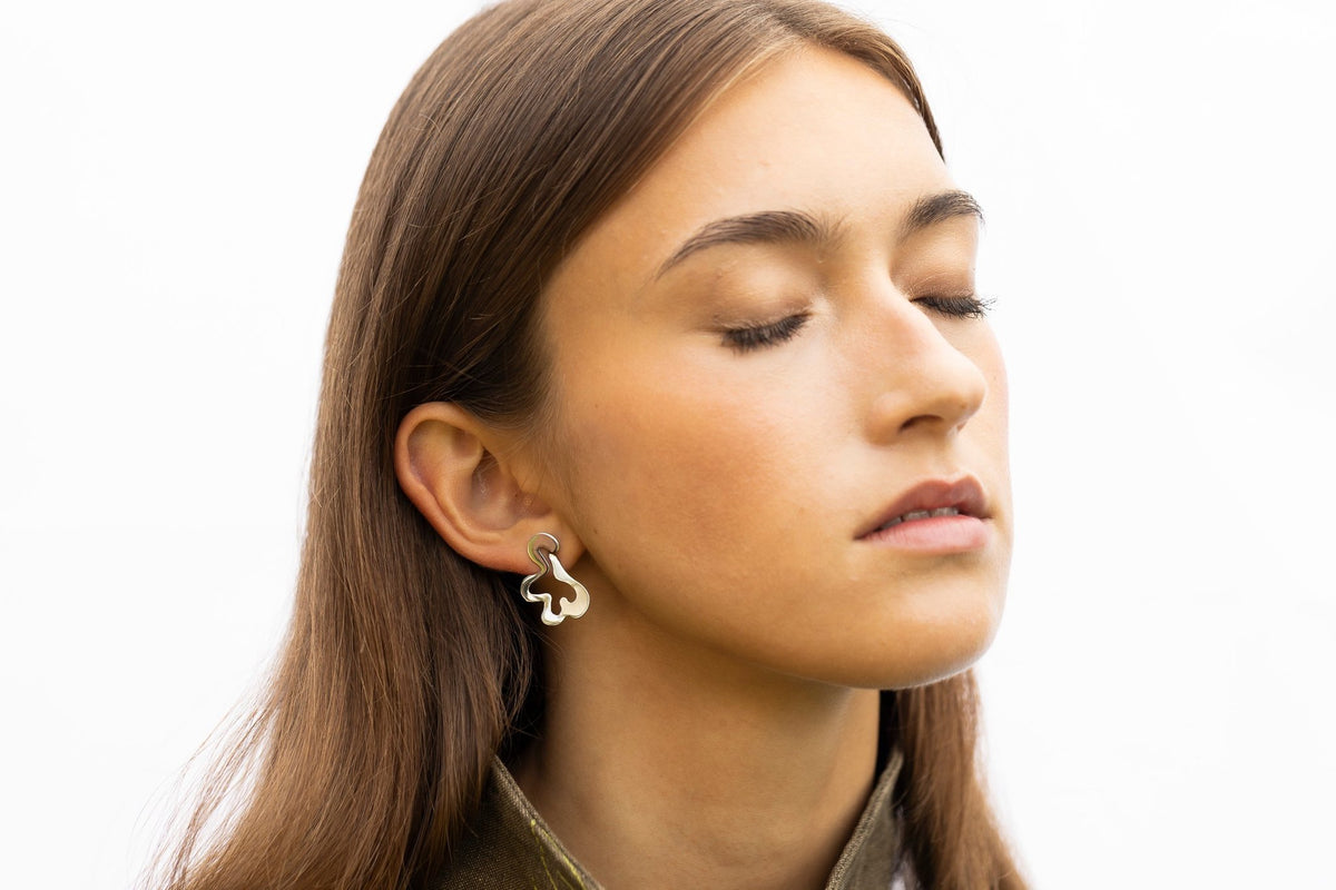1. Woman wearing Lentsius Folia Bold earrings with eyes closed, showcasing polished stainless steel design