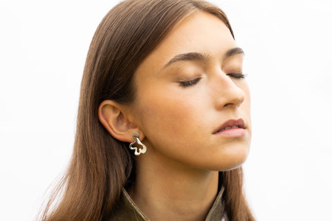1. Woman wearing Lentsius Folia Bold earrings with eyes closed, showcasing polished stainless steel design