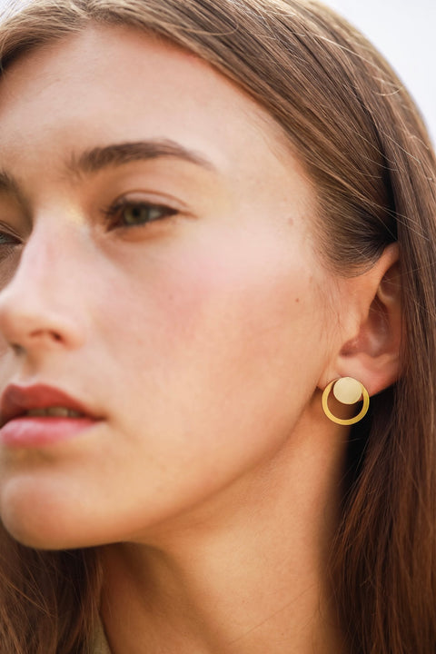 1. Close-up of woman wearing Lentsius Luna Sunlit earrings with gold circular design, shown in outdoor setting