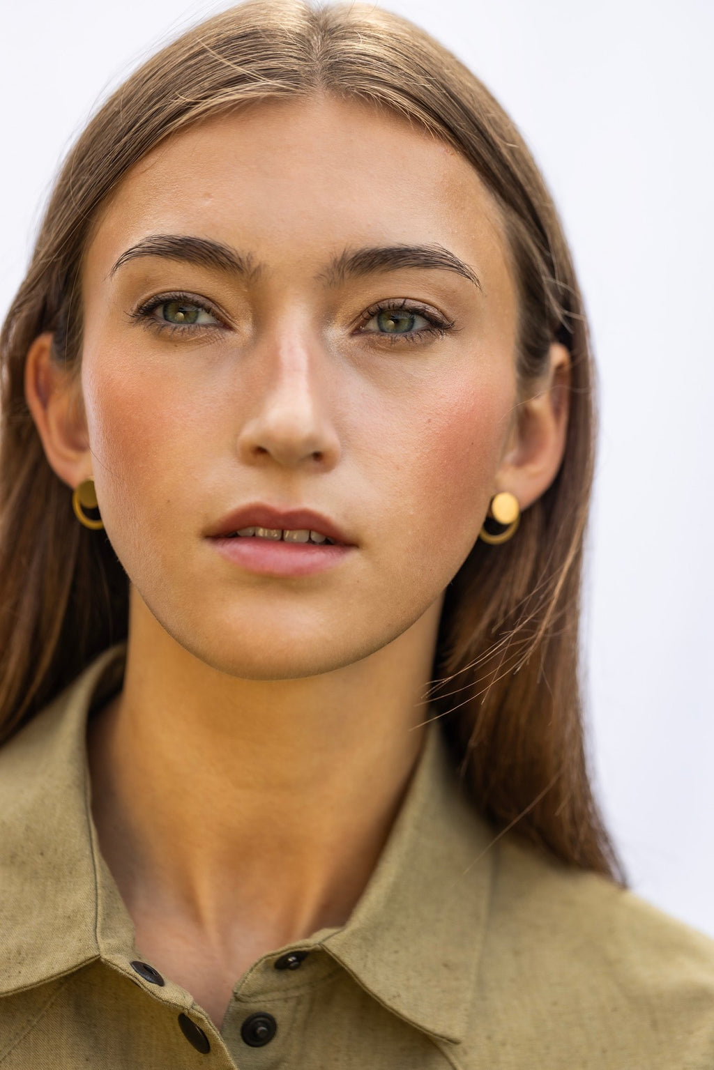 1. Woman wearing Lentsius Luna Sunlit earrings with gold circular design, shown in outdoor setting