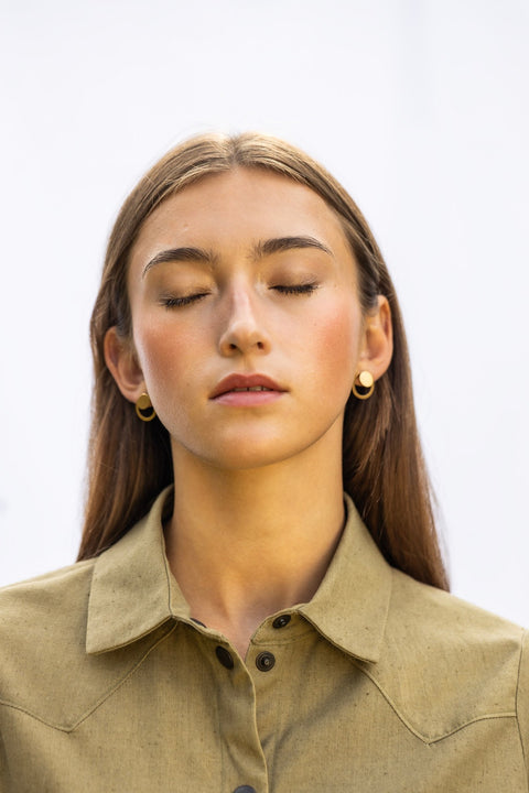 1. Woman wearing Lentsius Luna Sunlit earrings with gold circular design, eyes closed in outdoor setting