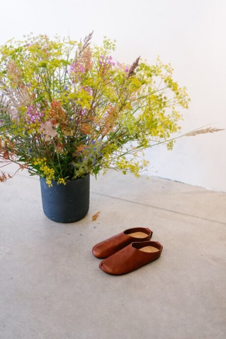 2. Kyoto brown slippers by Omaking placed on floor next to vibrant floral arrangement