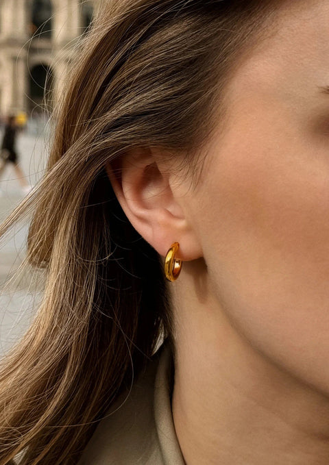 1. Woman wearing NO MORE Ella Hoops Earrings in gold, showcasing elegant style in a lifestyle setting