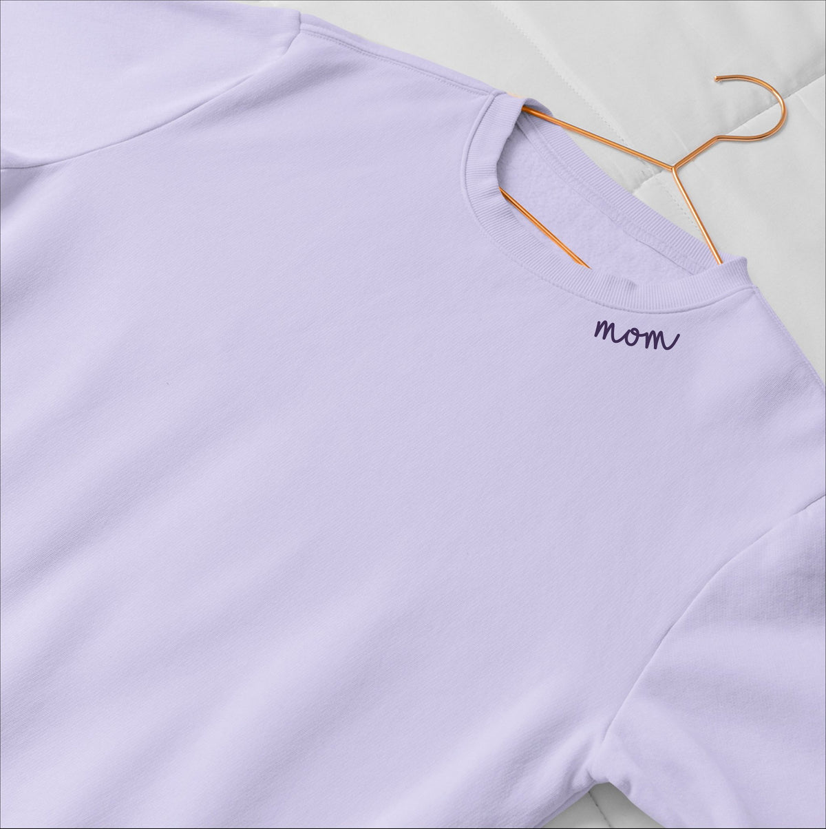 3. Lilac unisex organic cotton sweatshirt with 'Mom' embroidery on collar, laid flat on bed