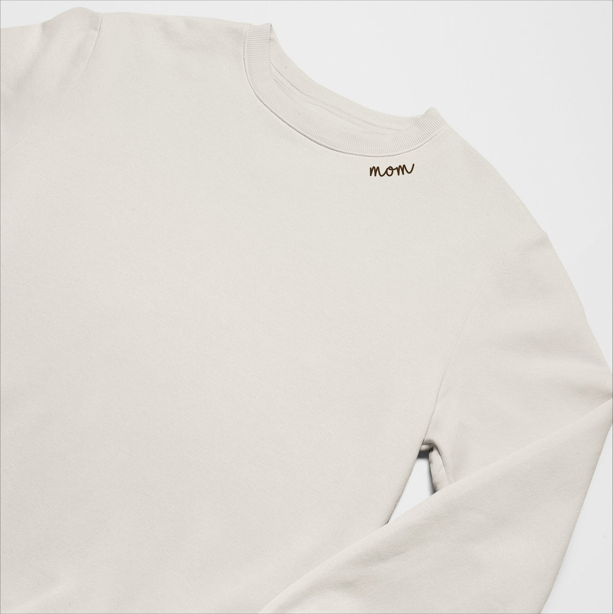 4. Beige unisex organic cotton sweatshirt with 'Mom' embroidery on collar, laid flat